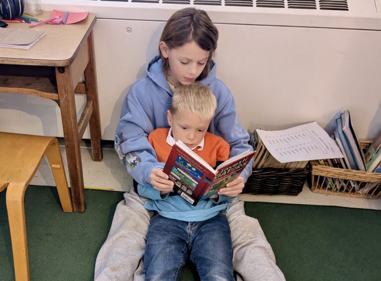 An older student reads to a younger student during a partner class